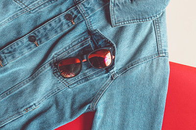 Sonnenbrille in einer Jeansjackentasche auf einem farbigen b