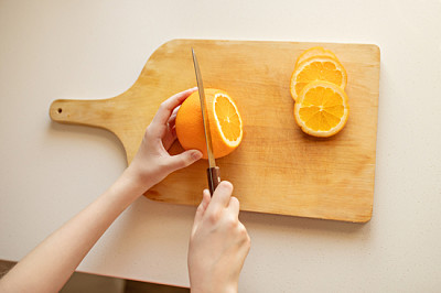 Hand, die Orange auf Holzbrett schneidet